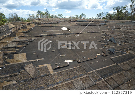 Wind damaged house roof with missing asphalt shingles after hurricane Ian in Florida. Repair of home rooftop concept Wind damaged house roof with missing asphalt shingles after hurricane Ian in Florida. Repair of home rooftop concept 112837319
