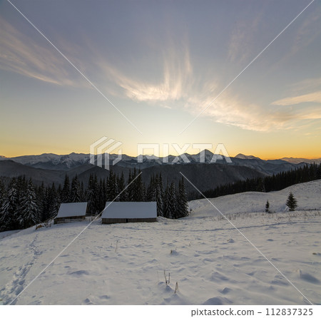 Old wooden house, hut and barn in deep snow on mountain valley, spruce forest, woody hills on clear blue sky at sunrise copy space background. Mountain winter panorama landscape. 112837325