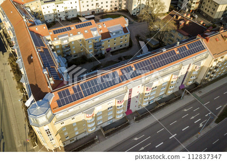 Top view of blue solar photo voltaic panels system on high apartment building roof top on sunny day. Renewable ecological green energy production concept. Top view of blue solar photo voltaic panels system on high apartment building roof top on sunny day. Renewable ecological green energy production concept. 112837347