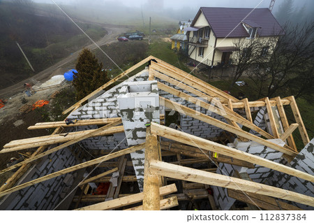 Top view of roof frame from wooden lumber beams and planks on walls made of hollow foam insulation blocks. Building, roofing, construction and renovation concept. 112837384