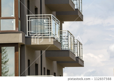 Close-up detail of apartment building wall with balconies and shiny windows on blue sky background. Close-up detail of apartment building wall with balconies and shiny windows on blue sky background. 112837388