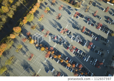 View from above of many parked cars on parking lot with lines and markings for parking places and directions. Place for vehicles in front of a strip mall center View from above of many parked cars on parking lot with lines and markings for parking places and directions. Place for vehicles in front of a strip mall center 112837397