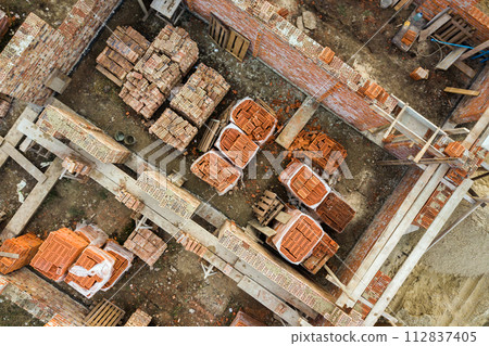 Aerial view of building site for future brick house, concrete foundation floor and stacks of yellow clay bricks for construction. 112837405