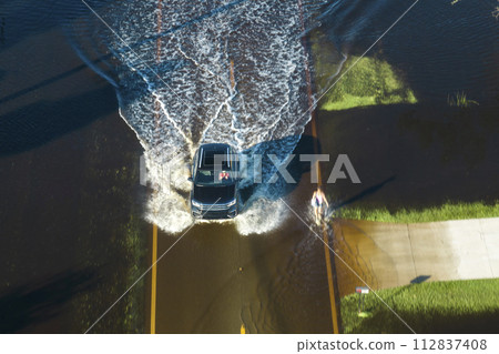 Hurricane flooded street with moving cars and surrounded with water houses in Florida residential area. Consequences of natural disaster Hurricane flooded street with moving cars and surrounded with water houses in Florida residential area. Consequences of natural disaster 112837408