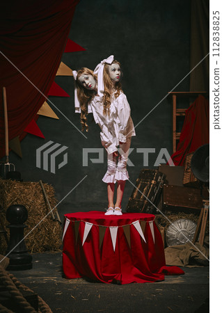 Siamese twin girls in white vintage costumes with makeup standing over dark retro circus backstage background. Creative spooky play 112838825