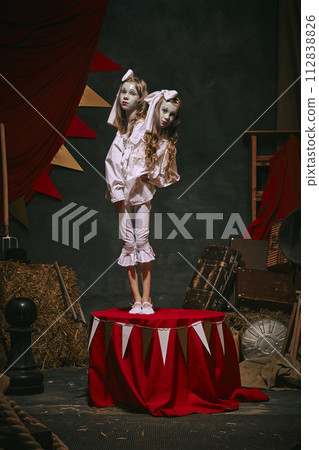 Siamese twin girls in white vintage costumes with makeup standing over dark retro circus backstage background. Creative spooky play 112838826