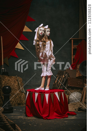 Siamese twin girls in white vintage costumes with makeup standing on stage over dark retro circus backstage background. 112838828