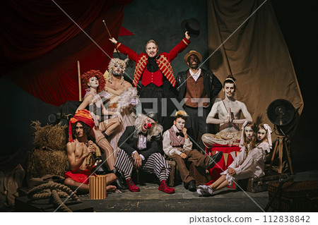 Diverse cast of vintage circus performers poses over dark retro circus backstage background. Promotional poster for upcoming performances. 112838842