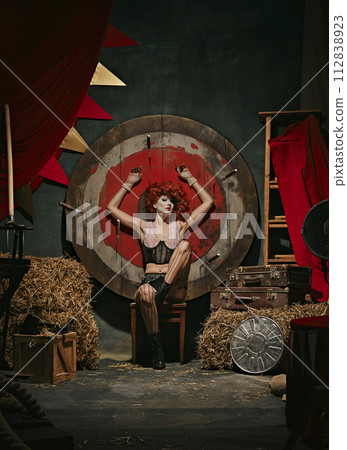 Woman in vintage costume and stage makeup poses before target over dark retro circus backstage background. Theatrical play 112838923