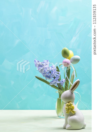 Turquoise Easter card. Color decorative eggs, ceramic bunny, jacinth flower in glass vase Copy space Turquoise Easter card. Color decorative eggs, ceramic bunny, jacinth flower in glass vase Copy space 112839135