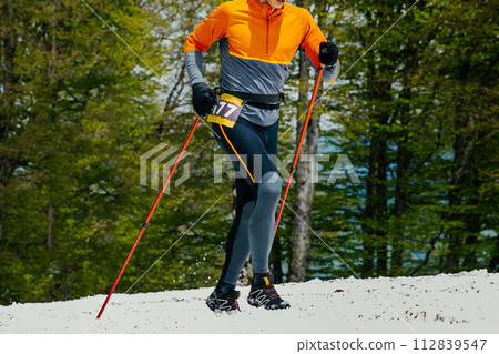 male athlete with trekking poles going uphill in snow during race 112839547