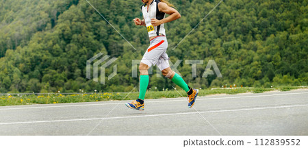 man athlete athlete running in background of green forest, compression sleeves on legs 112839552