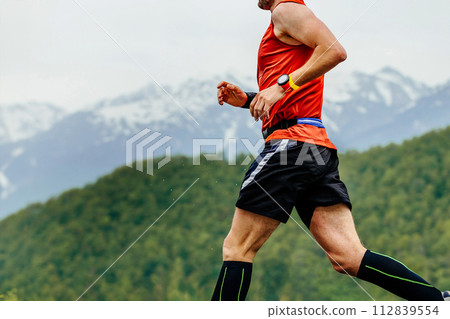 close-up man running in background of mountains and forests, with timer on his arm 112839554