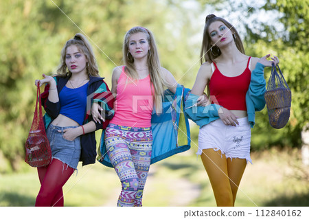Three beautiful country girls dressed in the style of the nineties are walking along the road. Three beautiful country girls dressed in the style of the nineties are walking along the road. 112840162