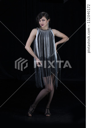 A beautiful girl dressed in the style of the 20-30s of the last century posing on a dark background. A beautiful girl dressed in the style of the 20-30s of the last century posing on a dark background. 112840172
