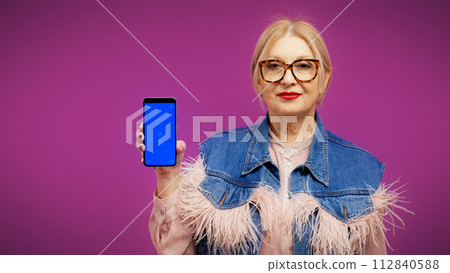 A pleased mature woman in trendy wear is showing a smartphone display, online document management A pleased mature woman in trendy wear is showing a smartphone display, online document management 112840588