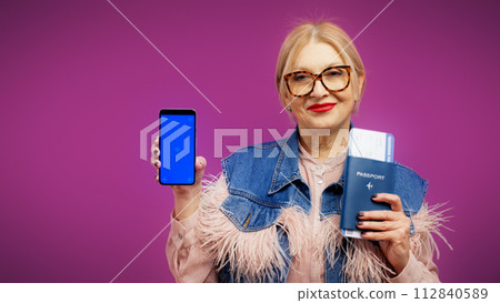 A senior woman is holding her passport with tickets and a phone, an online booking app A senior woman is holding her passport with tickets and a phone, an online booking app 112840589