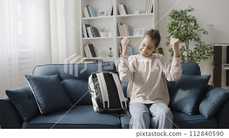 Excited teenager showing yes gesture, sitting with backpack on sofa, good news Excited teenager showing yes gesture, sitting with backpack on sofa, good news 112840590