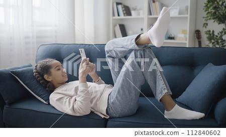 Smiling teenage girl chatting with friends online at home, using smartphone app Smiling teenage girl chatting with friends online at home, using smartphone app 112840602