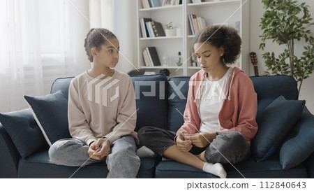 Black teenage girl telling bad news to best friend at home, sharing a secret 112840643
