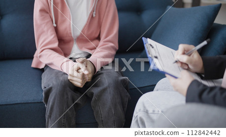 Doctor writing notes on clipboard, sitting near young patient, teen counselling Doctor writing notes on clipboard, sitting near young patient, teen counselling 112842442