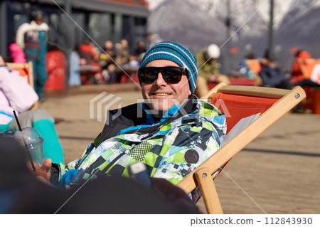 Smiling man in ski gear enjoying a beverage during a break at a ski resort. 112843930