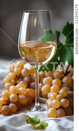 Glass of white wine half full with a few leaves from the vine and white grapes 112845174