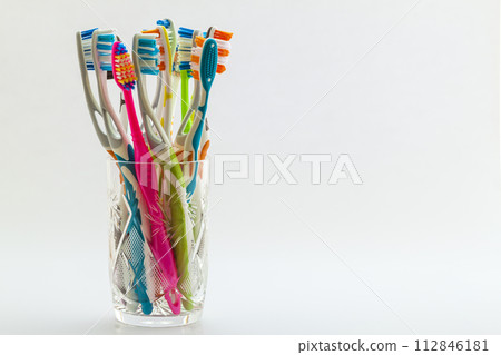 Close up shot of set of multicolored toothbrushes in glass on clean toilet on white background, concept dental. Close up shot of set of multicolored toothbrushes in glass on clean toilet on white background, concept dental. 112846181