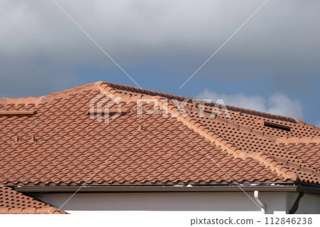Tiled roof covering of condo building in Florida. Closeup of house rooftop covered with ceramic shingles Tiled roof covering of condo building in Florida. Closeup of house rooftop covered with ceramic shingles 112846238