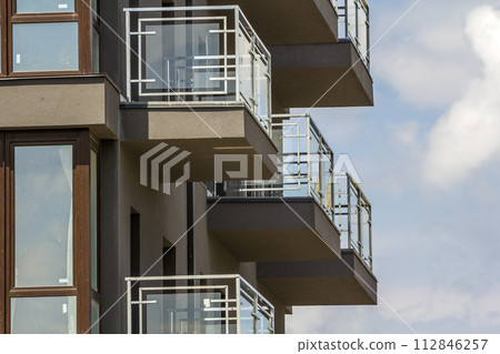 Close-up detail of apartment building wall with balconies and shiny windows on blue sky background. 112846257