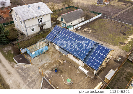 Aerial top view of new modern residential house cottage with blue shiny solar photo voltaic panels system on roof. Renewable ecological green energy production concept. 112846261