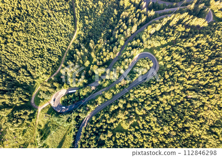 Aerial view of winding road in high mountain pass trough dense green pine woods. 112846298