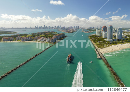 View from above of big container ship entering main channel in Miami harbor near South Beach high luxurious hotels and apartment buildings View from above of big container ship entering main channel in Miami harbor near South Beach high luxurious hotels and apartment buildings 112846477