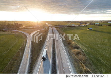 Aerial view of modern highway road intersection at dawn on rural landscape and raising sun background. Drone photography. 112846495