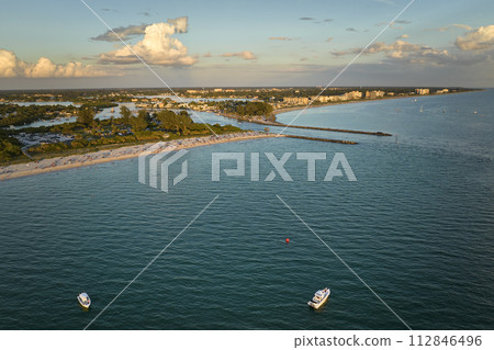Aerial view of sea shore near Venice, Florida with white yachts at sunset floating on sea waves. North and South Jetty on Nokomis beach. Motor boat recreation on ocean surface 112846496