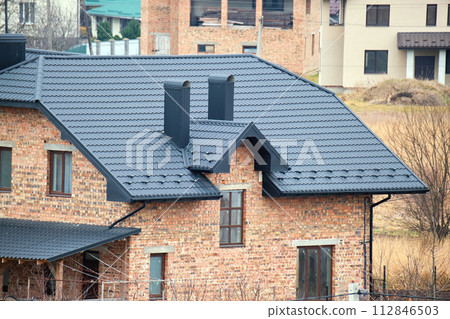 Chimney on house roof top covered with metallic shingles under construction. Tiled covering of building. Real estate development Chimney on house roof top covered with metallic shingles under construction. Tiled covering of building. Real estate development 112846503