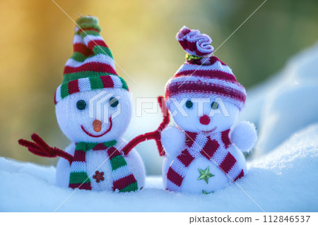 Two small funny toys baby snowman in knitted hats and scarves in deep snow outdoors on bright blue and white copy space background. Happy New Year and Merry Christmas greeting card. Two small funny toys baby snowman in knitted hats and scarves in deep snow outdoors on bright blue and white copy space background. Happy New Year and Merry Christmas greeting card. 112846537