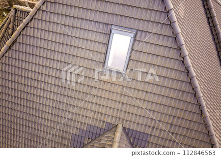Close-up of new attic plastic window installed in shingled house roof. Professionally done building and construction work, roofing and installation concept. Close-up of new attic plastic window installed in shingled house roof. Professionally done building and construction work, roofing and installation concept. 112846563