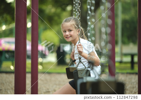 Young pretty smiling teenage girl playing alone on swings on summer playground Young pretty smiling teenage girl playing alone on swings on summer playground 112847298