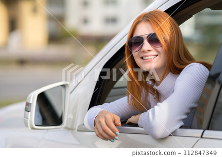 Young woman with red hair driving a car. 112847349