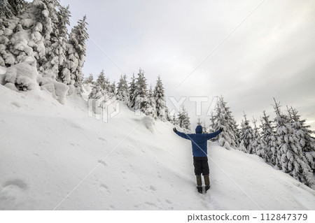 Back view of tourist hiker standing with raised arms on steep mountain slope on copy space background of spruce trees and clear sky. Tourism and winter mountain sports concept. Back view of tourist hiker standing with raised arms on steep mountain slope on copy space background of spruce trees and clear sky. Tourism and winter mountain sports concept. 112847379