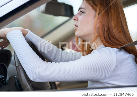 Sad tired yound woman driver sitting behind the car steering wheel in traffic jam. 112847406