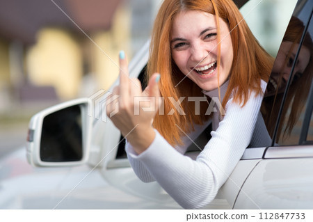 Pissed off displeased angry aggressive woman driving a car shouting at someone with middle finger gesture. 112847733