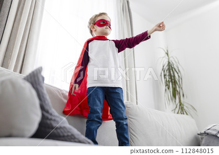 Young boy in superhero costume playing at home. 112848015