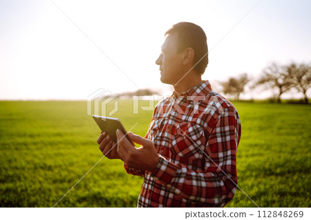 Farmer working with digital tablet in field at sunset. Checking wheat field. Agriculture concept. 112848269