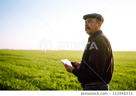 Farmer owner using touchpad for check wheat field at sunset. Farmer working with digital tablet. Farmer owner using touchpad for check wheat field at sunset. Farmer working with digital tablet. 112848311