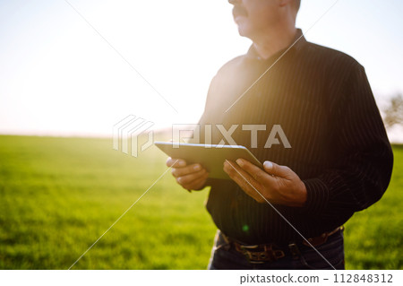 Farmer owner using touchpad for check wheat field at sunset. Farmer working with digital tablet. 112848312