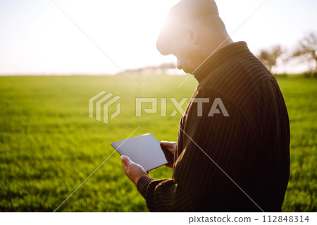 Farmer owner using touchpad for check wheat field at sunset. Farmer working with digital tablet. Farmer owner using touchpad for check wheat field at sunset. Farmer working with digital tablet. 112848314