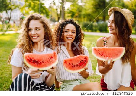 Cheerful happy friends camping on the grass, eating watermelon, laughing. Cheerful happy friends camping on the grass, eating watermelon, laughing. 112848829