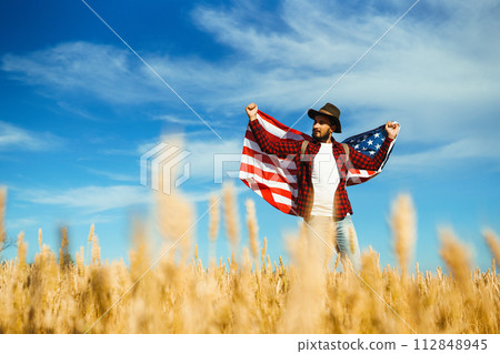 4th of July. American Flag. Traveler with the flag of America. The man in a hat, a backpack, a shirt and jeans. 4th of July. American Flag. Traveler with the flag of America. The man in a hat, a backpack, a shirt and jeans. 112848945